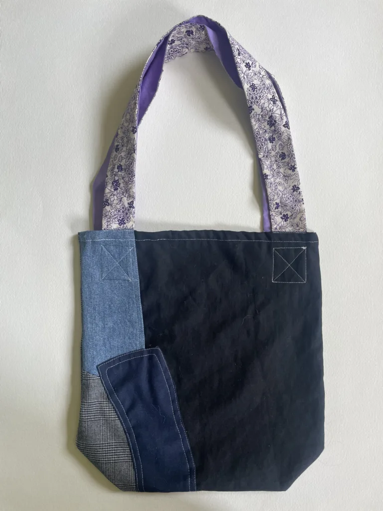 Back view of the patchwork tote showing its denim panel and floral-print straps