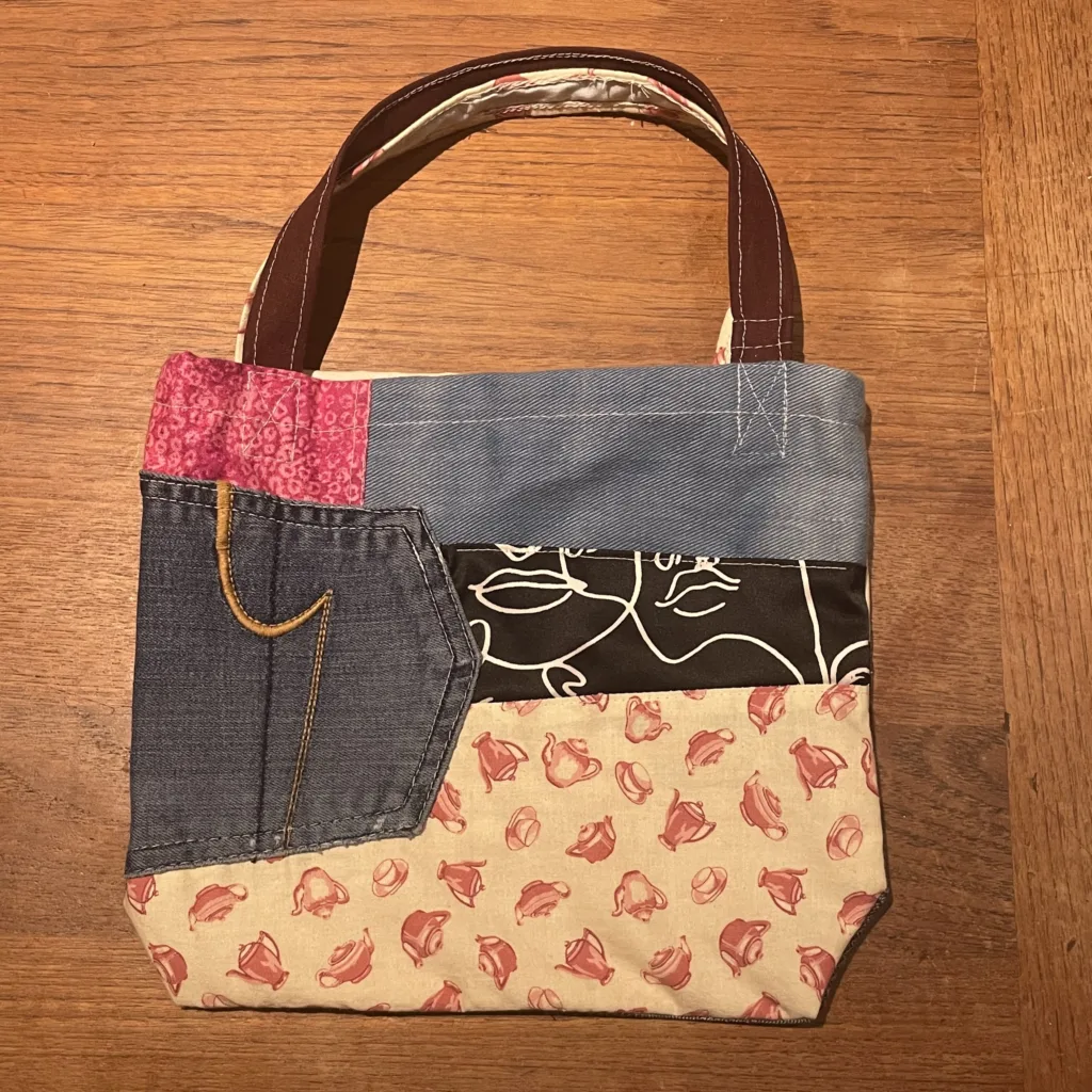 Small patchwork tote bag pieced from denim, floral and printed fabric scraps with brown handles